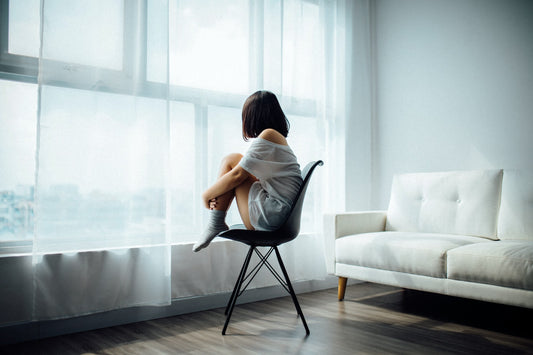 Woman sits alone in a gray room, looking out the window